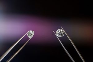 Two tweesers hold diamonds, on the left an uncut rough diamond; on the right, a brilliant, cut stone glistening with facets.