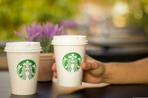 Two Starbucks coffee cups and a hand reaching across the photo holding one slightly up