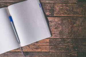 A journal notebook laying open on a wooden table with a pen resting inside the spine