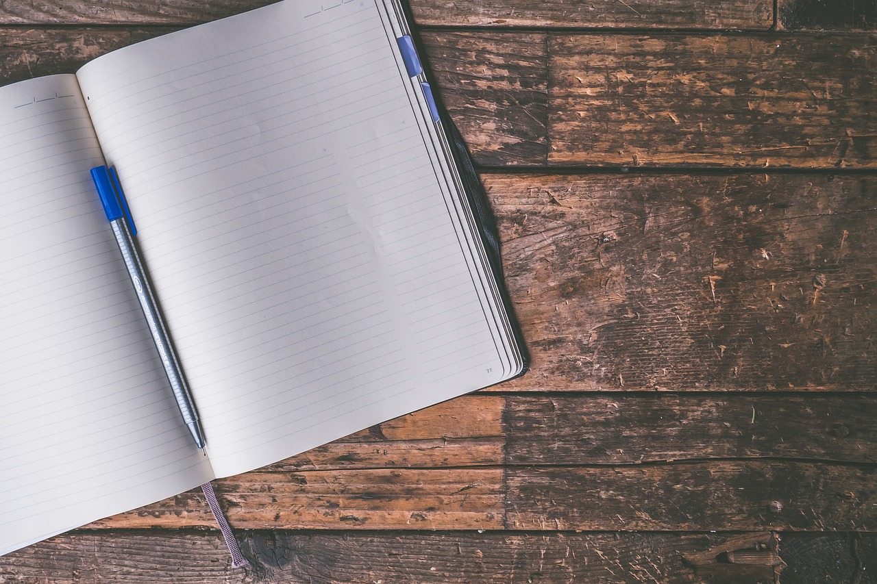 A journal notebook laying open on a wooden table with a pen resting inside the spine