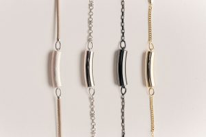 Four pieces of jewelry, each a different shiny titanium, necklaces on chains, curved cylinders, AI-enabled jewelry from Nirva