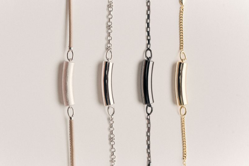 Four pieces of jewelry, each a different shiny titanium, necklaces on chains, curved cylinders, AI-enabled jewelry from Nirva